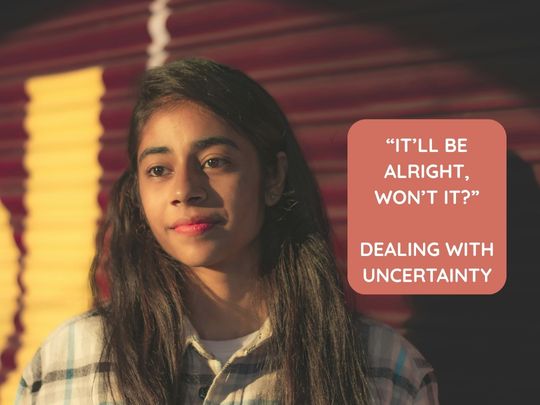 Image of young brown-skinned woman with long brown hair in checked jacket stood in front of deep red and yellow garage door. A text box reads: '"It'll be alright, won't it?' Dealing with uncertainty."